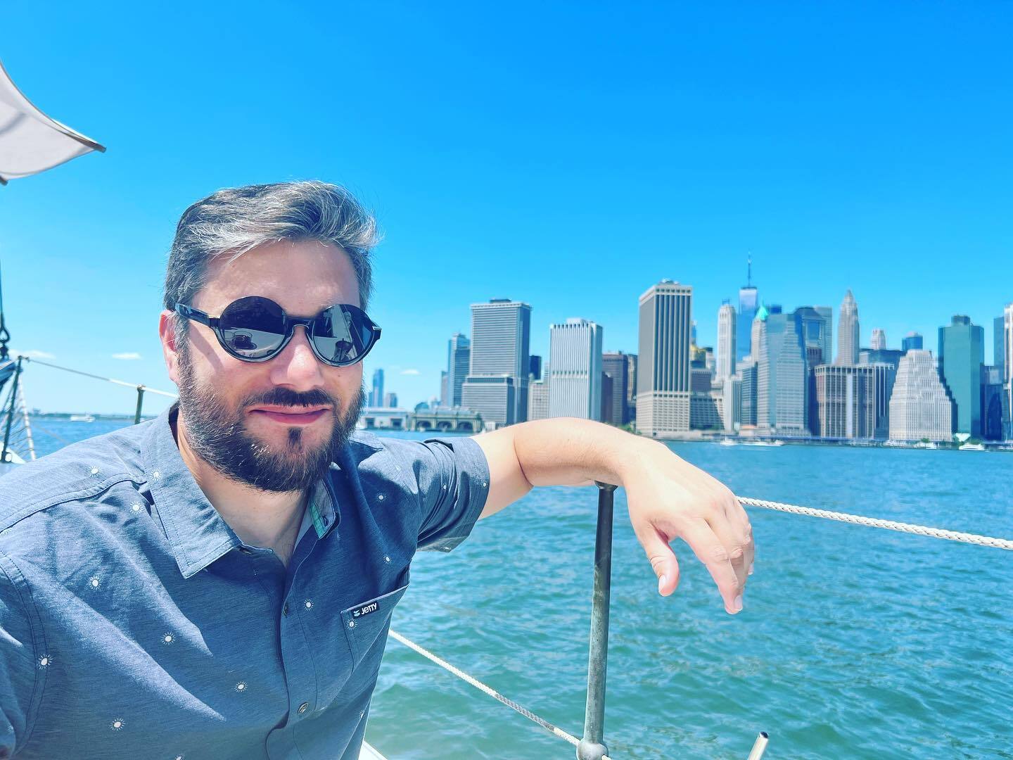 Un hombre de gafas de sol está sentado en un bote frente a la línea del cielo en la parte inferior de Manhattan