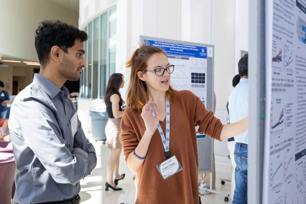 Una estudiante de posgrado hablando con un estudiante de posgrado sobre su póster de investigación científica para continuar su educación.