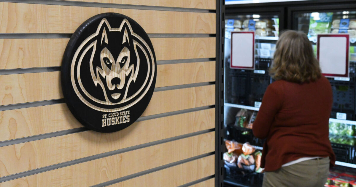 Un logotipo negro de St. Cloud State Huskies es visible contra los paneles de madera mientras una mujer mira hacia la sección del congelador.