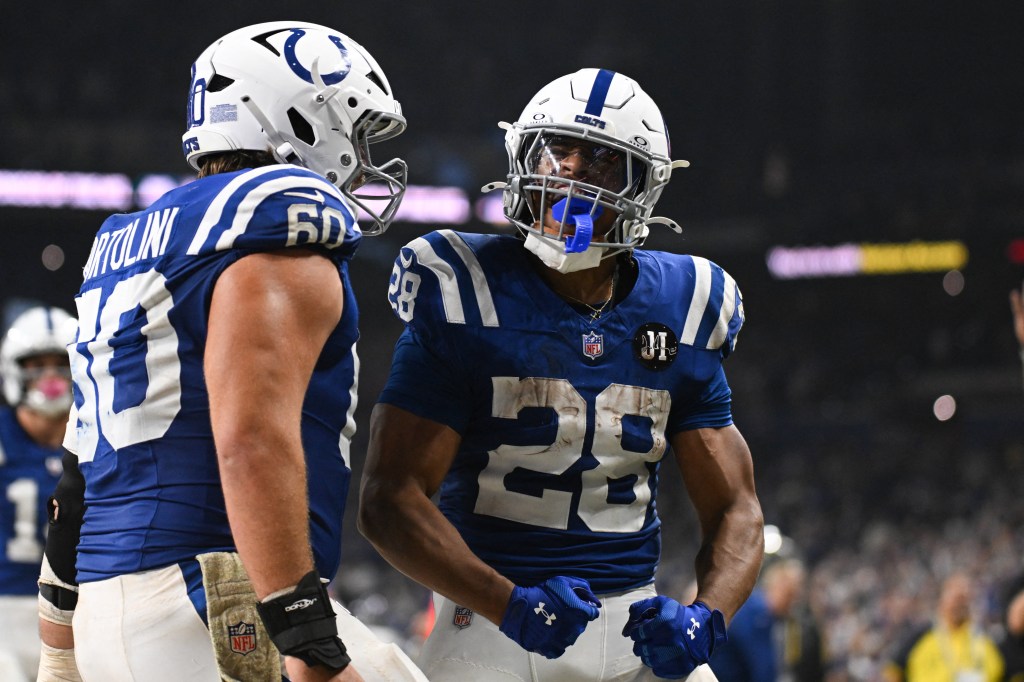 Dos jugadores de fútbol de los Indianapolis Colts uniformados, uno con la camiseta número 60 y el otro con el número 28, de pie en el campo.