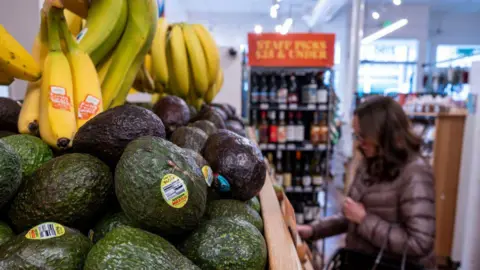 Aguacates y plátanos en una tienda de comestibles en San Francisco, California, EE. UU., con un hombre con un abrigo acolchado al fondo a través de Bloomberg Getty Images