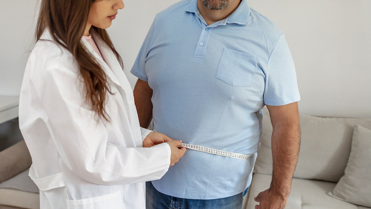 La doctora mide a un paciente masculino obeso.
