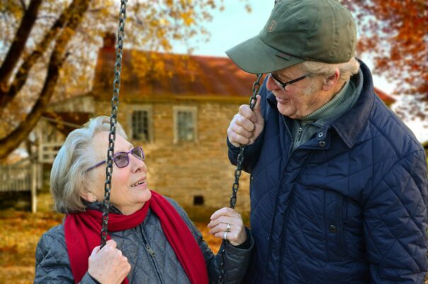 Anciano de pie junto a una anciana en columpio