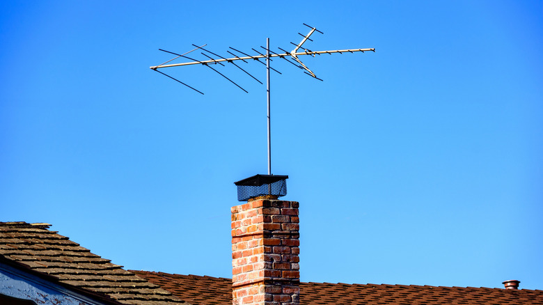Una antena de televisión tradicional está montada junto a una chimenea de ladrillo sobre un techo a cuatro aguas.