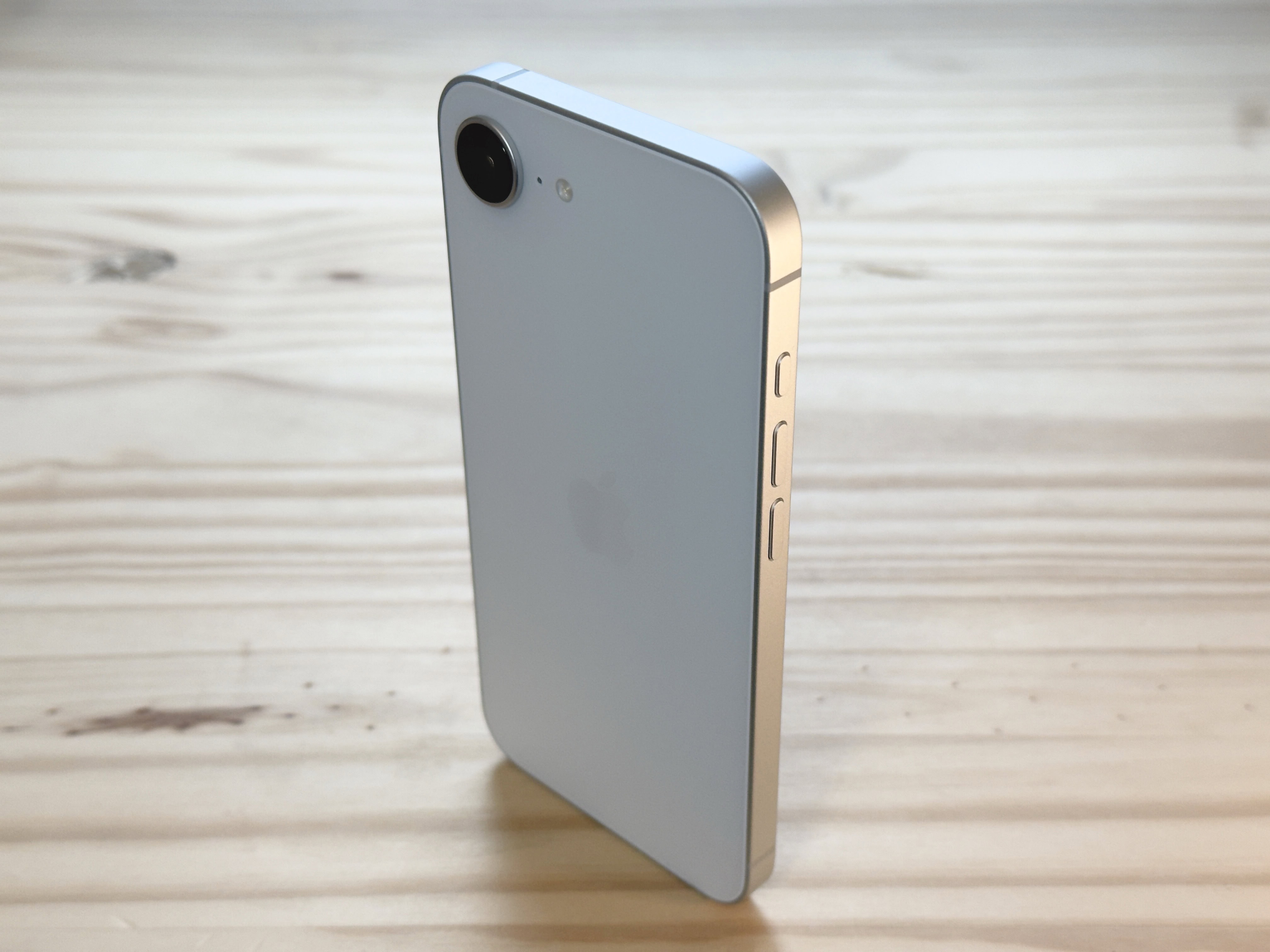 iPhone 16e de pie verticalmente sobre una superficie de mesa de pino, usado para ilustrar una revisión del iPhone 16e