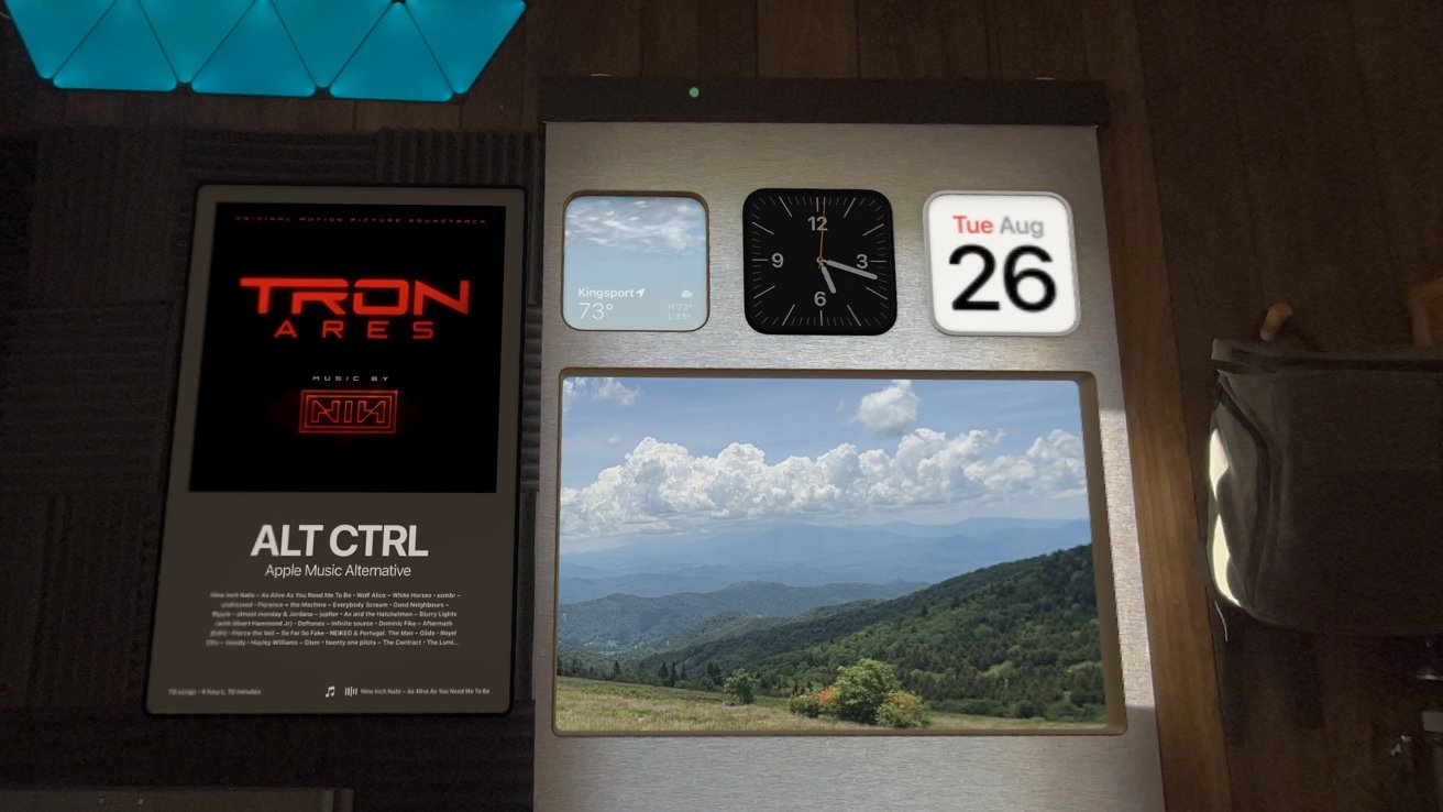 Pantalla digital con el tiempo (73F), reloj, calendario (26 de agosto), pintoresco paisaje montañoso y portada de la banda sonora de 'Tron Ares' sobre fondo negro.