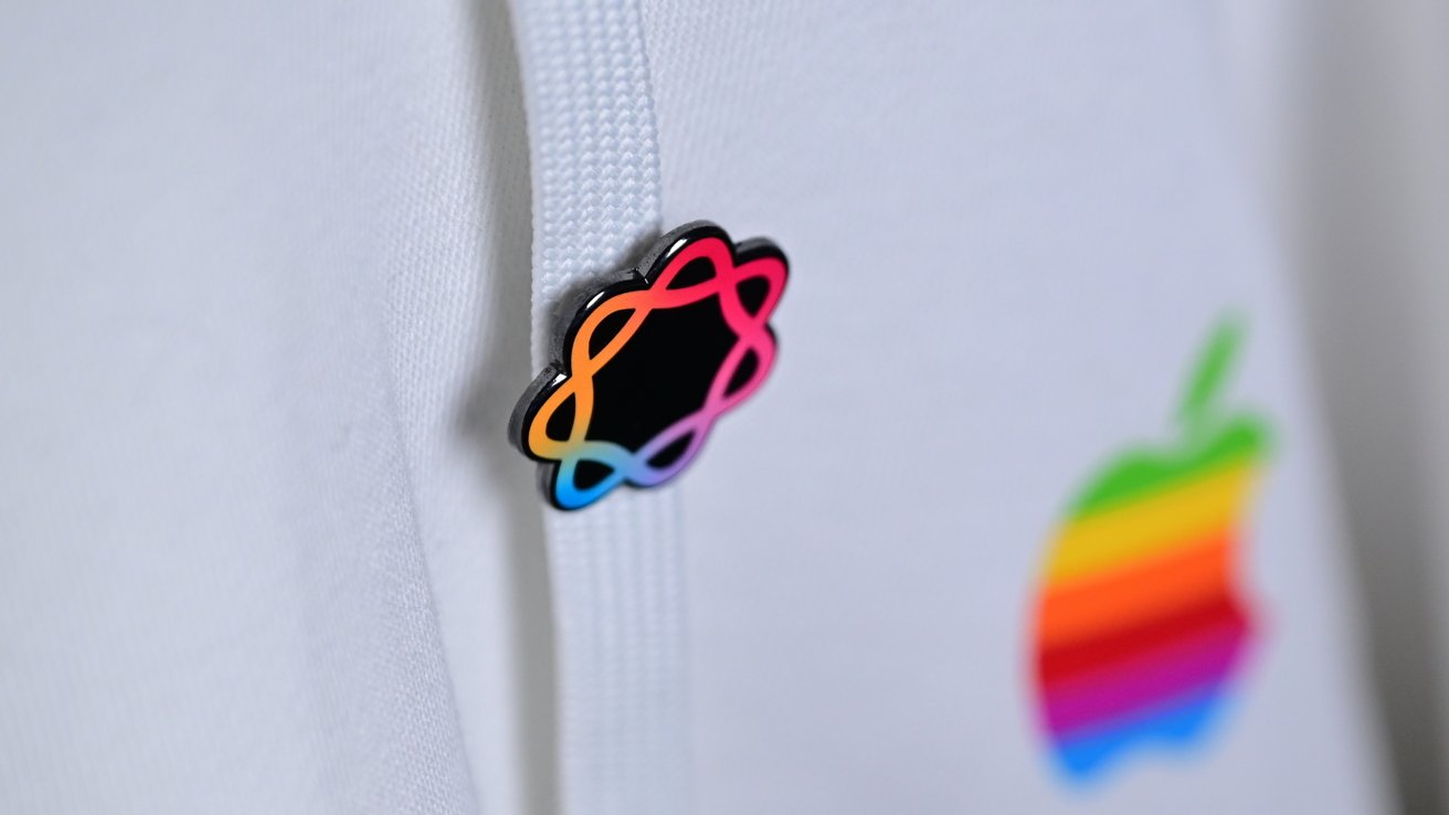 Primer plano de una sudadera con capucha de tela blanca que presenta un pequeño broche de flor multicolor en el cordón y un logotipo de Apple borroso con rayas de arcoíris en el fondo.