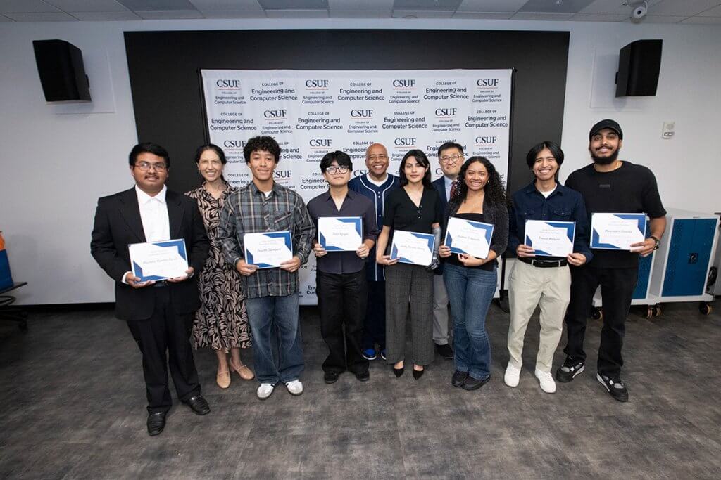 Foto grupal de estudiantes de pie en un salón de clases con certificados con miembros del cuerpo docente frente al fondo de la Facultad de Ingeniería y Ciencias de la Computación.