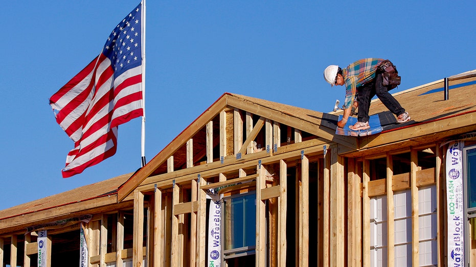 Trabajadores de la construcción construyendo una casa con una bandera estadounidense al fondo